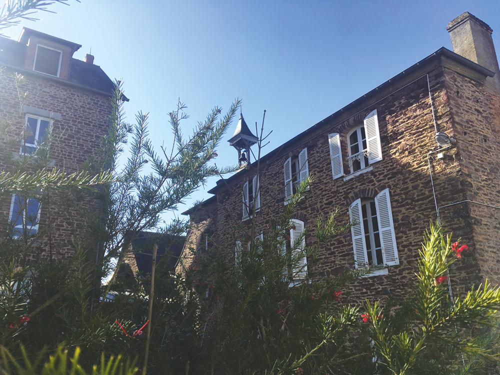 nous sommes dans la cour intérieure de l'ecole, l'IME et on voit un gros plan d'un des bâtiments de schiste.
On voit également la cloche de l'ancienne chapelle qui apparaît au-dessus du toit 